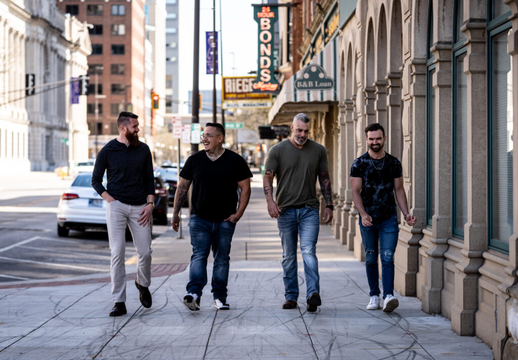 Four men walking together and laughing on a city sidewalk, representing men’s self improvement, brotherhood, and community.