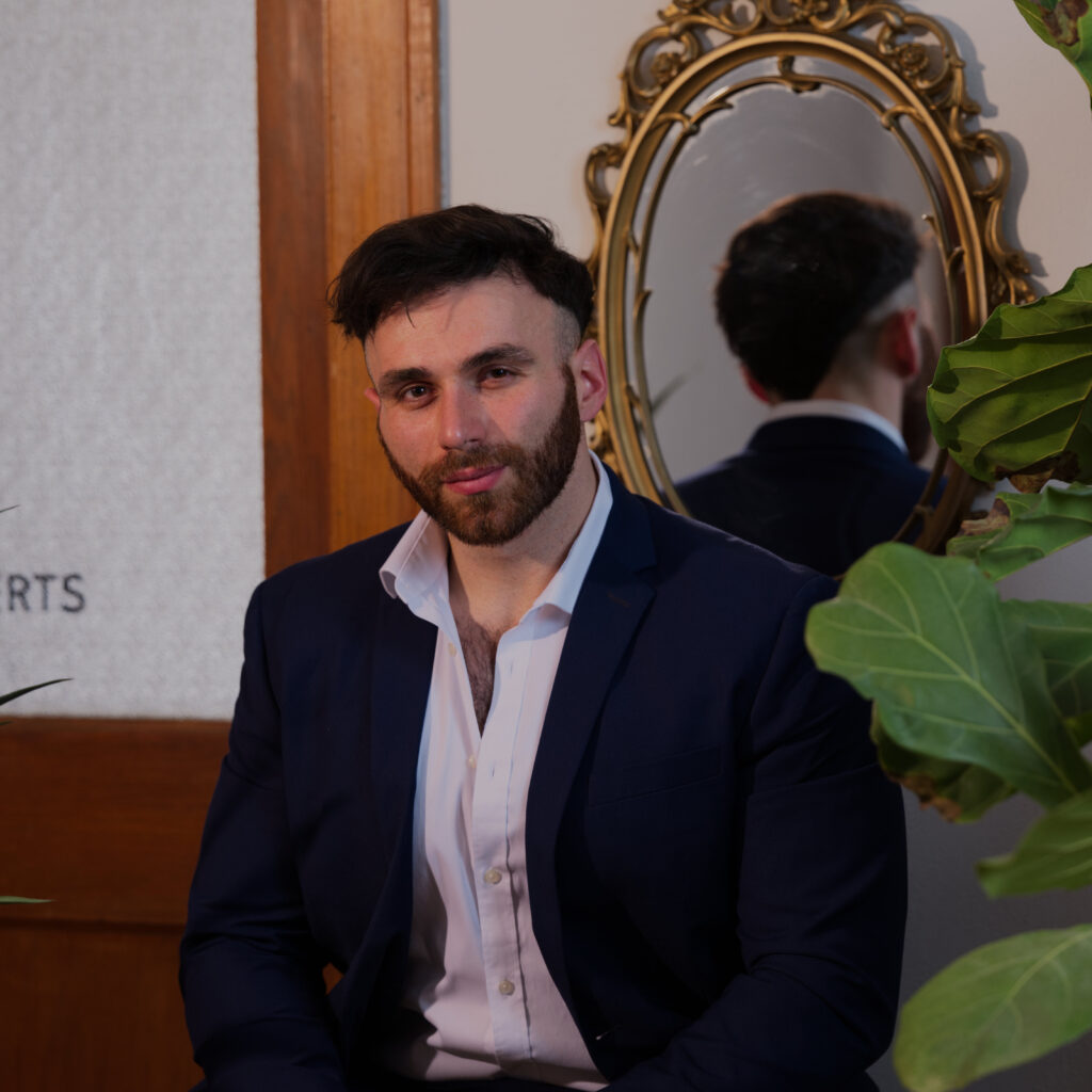 Man in a navy blazer sitting in front of a mirror, representing men’s self improvement and building a positive mindset.
