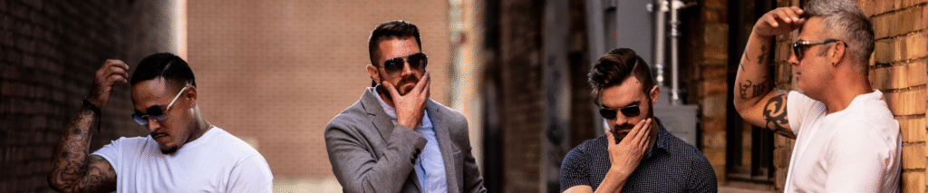Four men standing together in an urban alley, looking thoughtful and serious, representing self improvement for men and modern brotherhood.